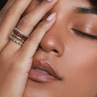 Close-up of a woman's face with one hand covering her eye, wearing multiple rings.