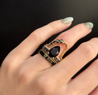 Gold ring with a black gemstone on a hand against a dark background