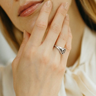 woman holding hand against her chin with a silver signet ring on ring finger